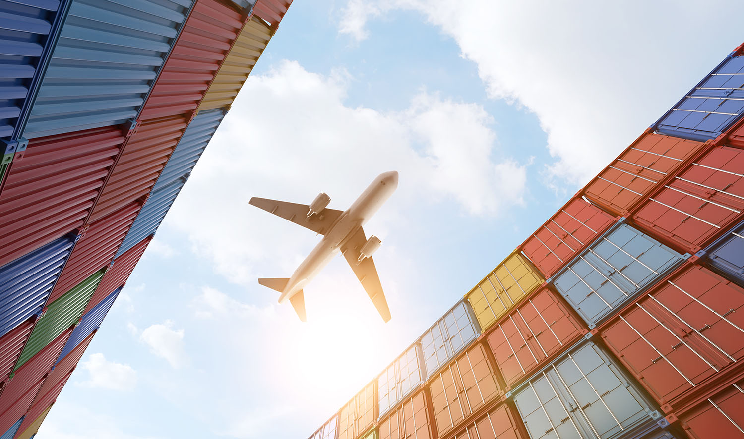 Cargo plane flying above stack of containers at container port